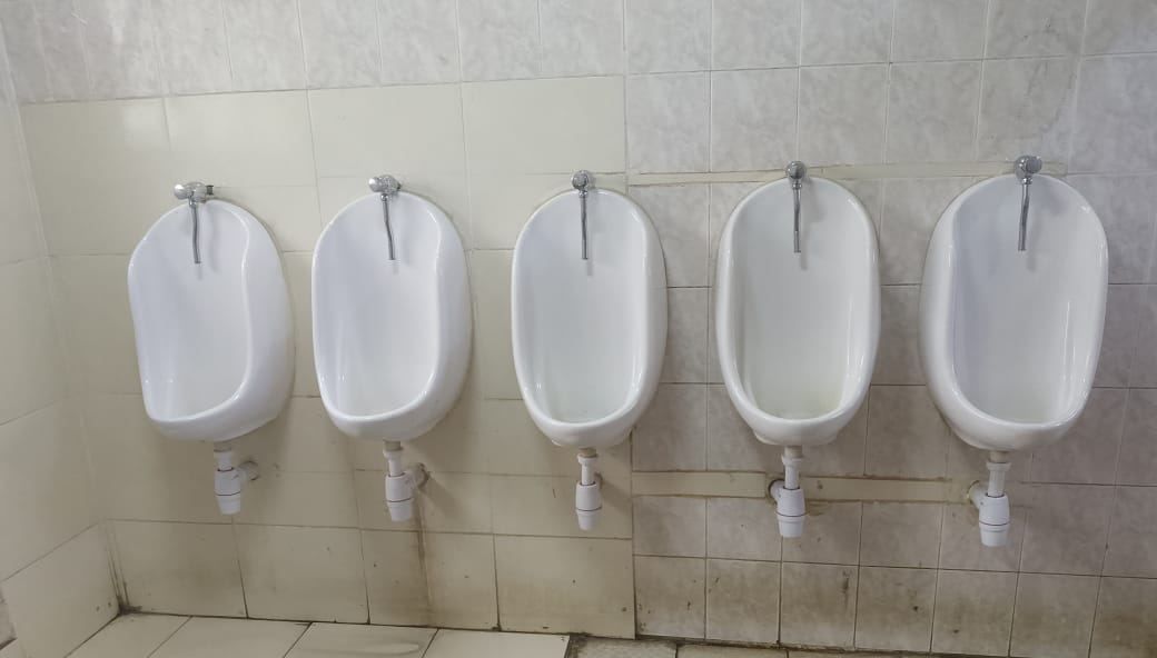 Row of five wall-hung urinals with new flush valves and waste traps in a commercial washroom